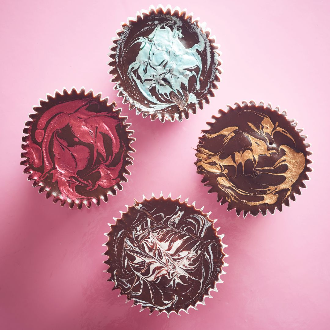 Four cupcakes with metallic marbled buttercream in pink, blue, bronze and silver