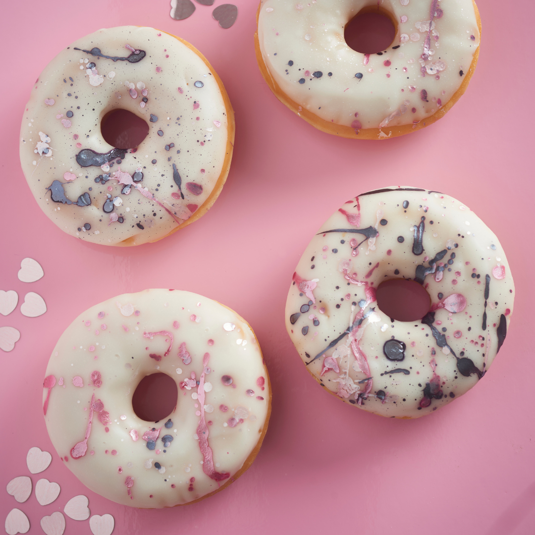 Four white-glazed doughnuts with pink, purple and metallic marbled decoration