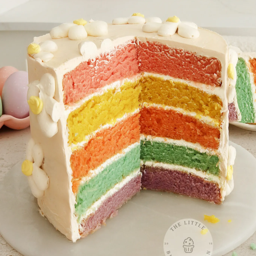 Sliced rainbow layer cake with white buttercream and pastel marshmallow decoration