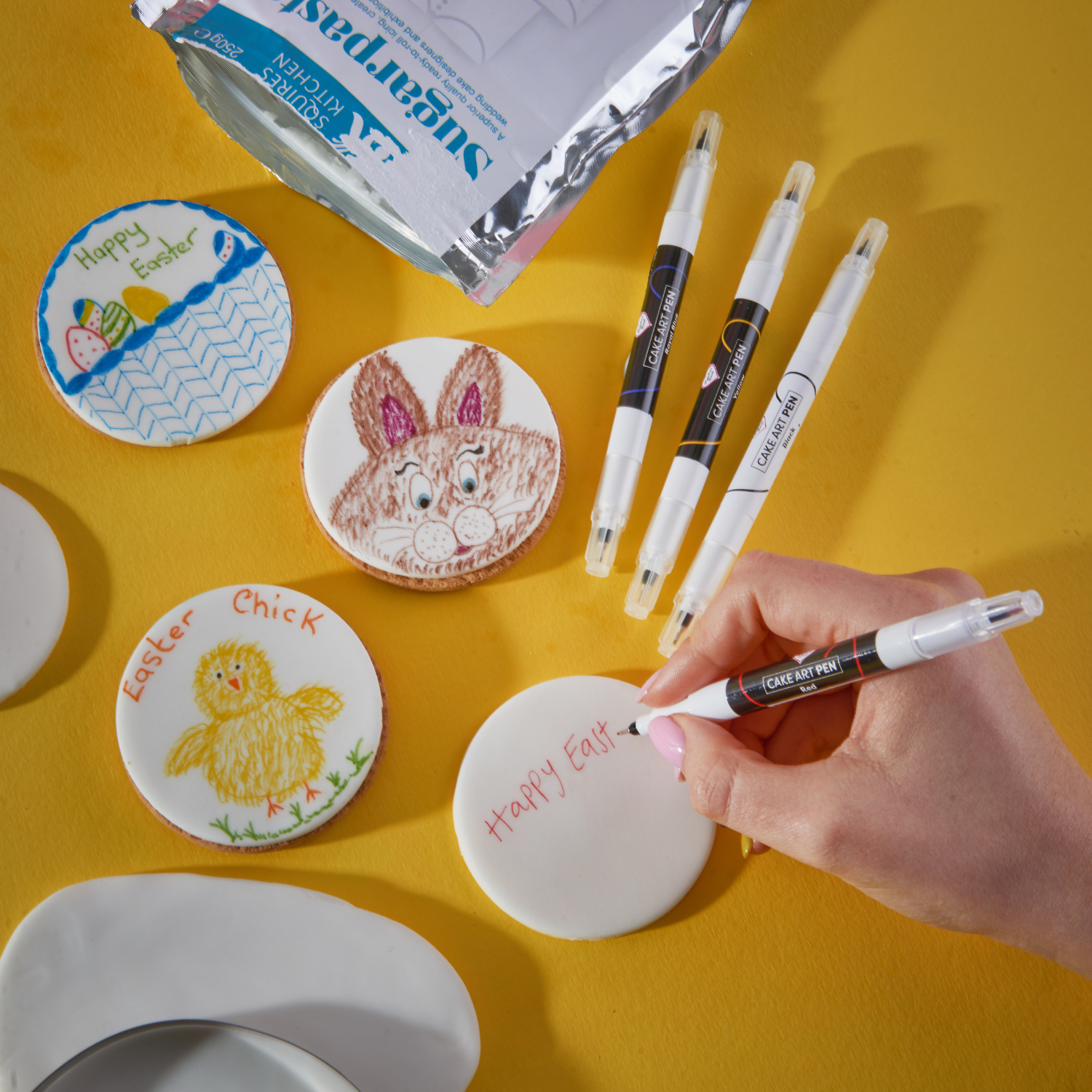 Easter biscuits being decorated with edible colouring pens on a yellow table