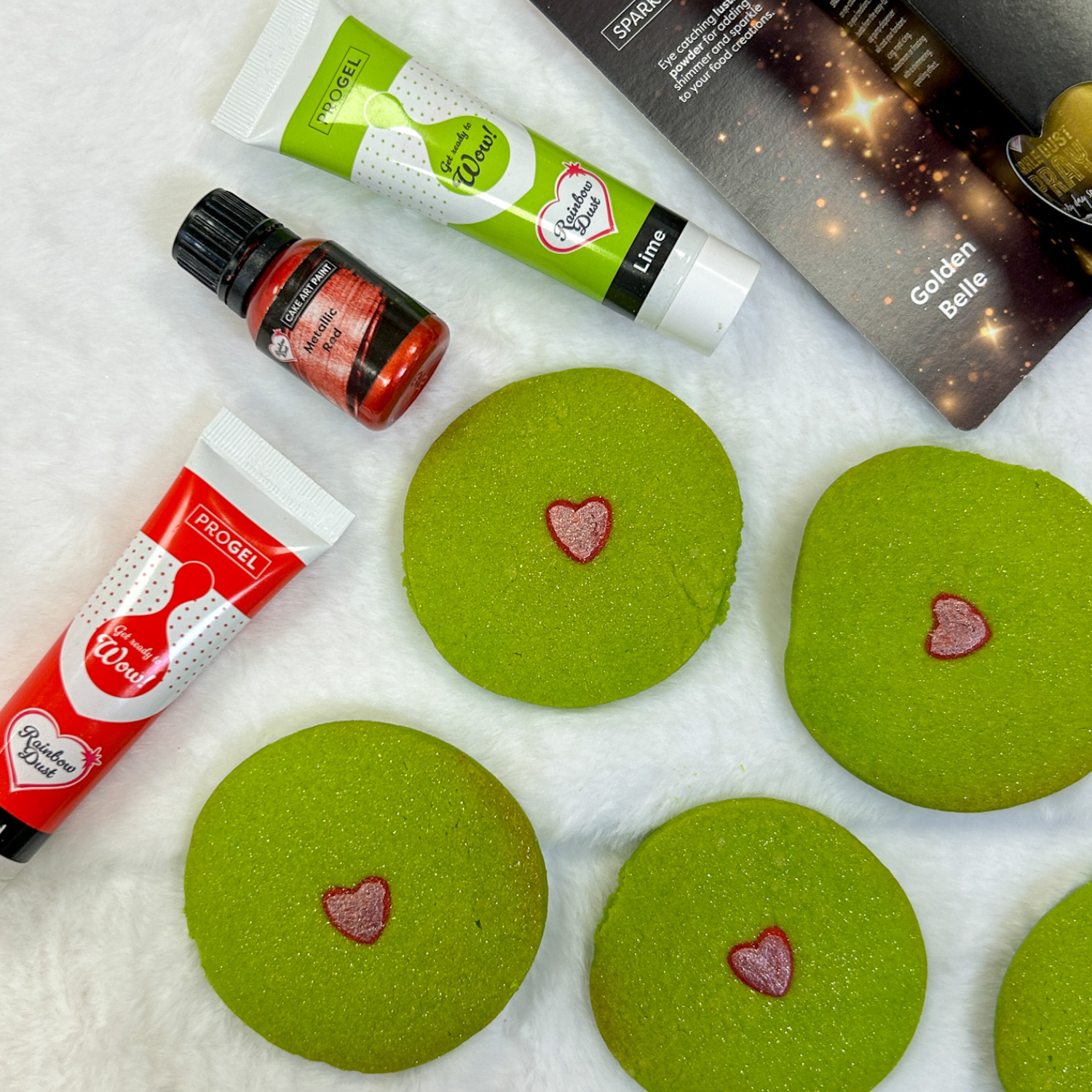 Green Grinch cookies with pink heart centres beside ProGel and gold leaf
