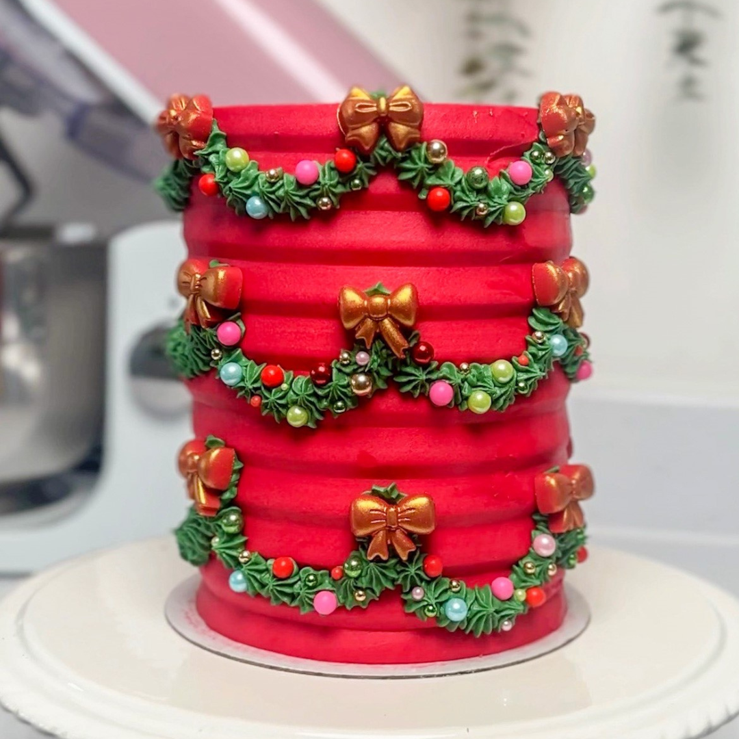 Red tiered Christmas cake decorated with green wreaths and gold bows