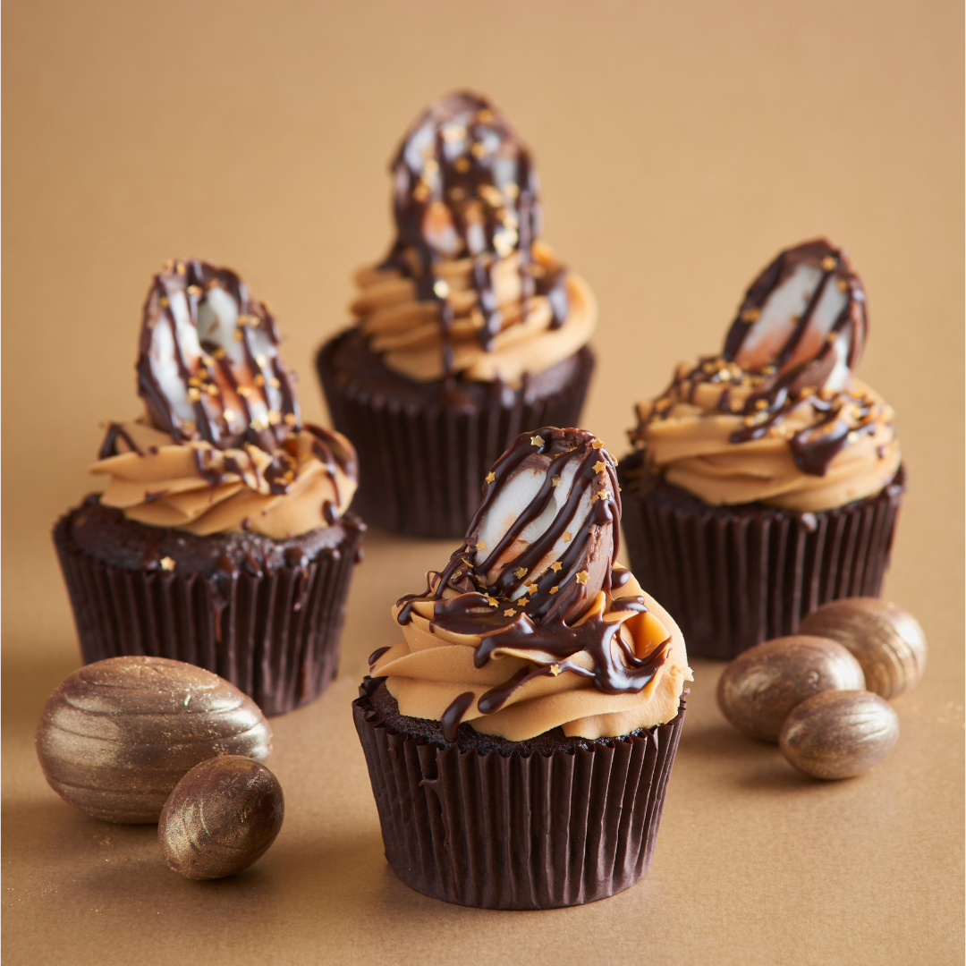 Four chocolate cupcakes topped with caramel buttercream, chocolate drizzle and half Easter eggs