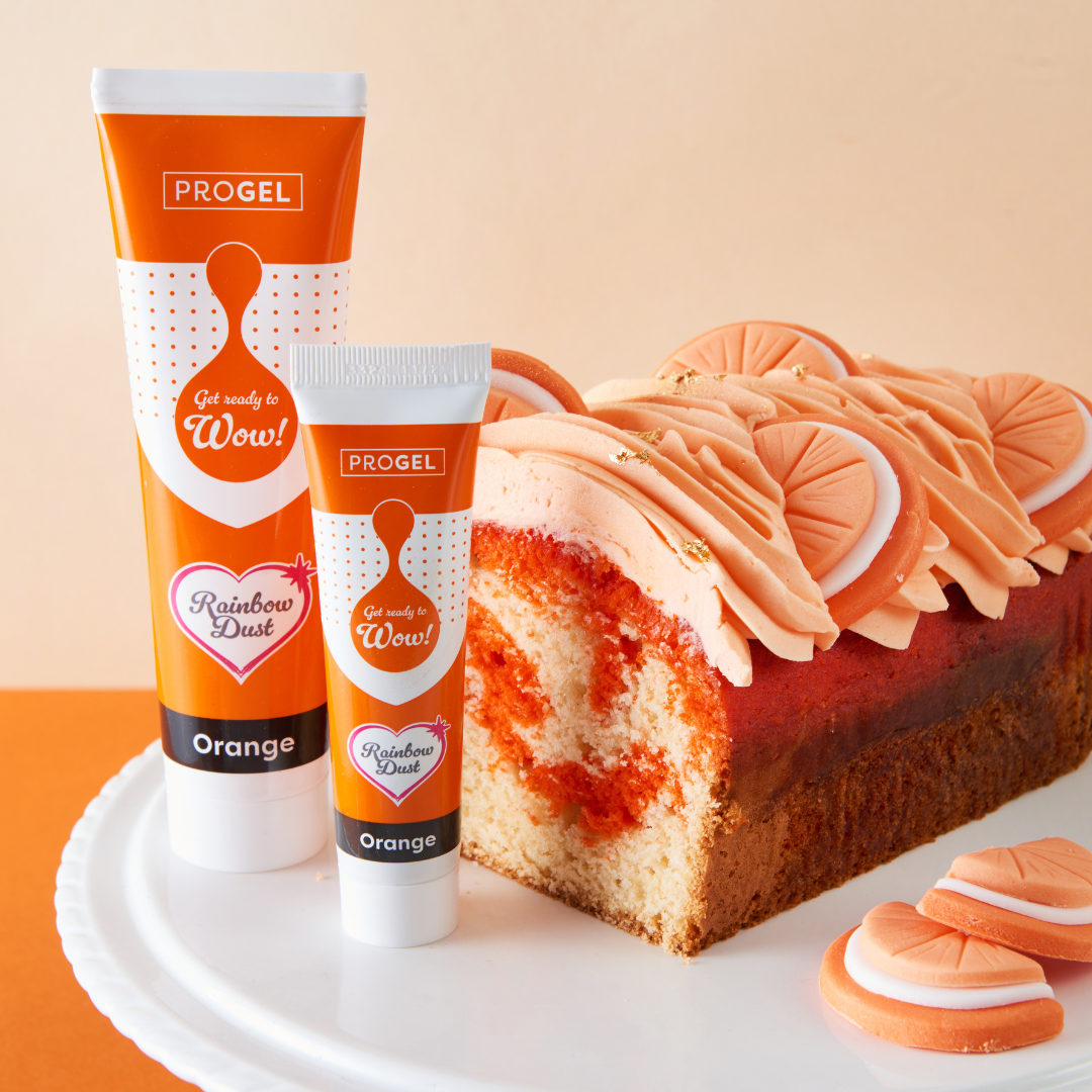 Orange ProGel tubes beside a sliced orange marbled loaf cake and iced cookies