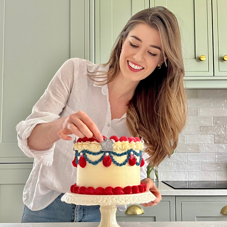 Woman holding a red, white and blue buttercream celebration cake in a kitchen
