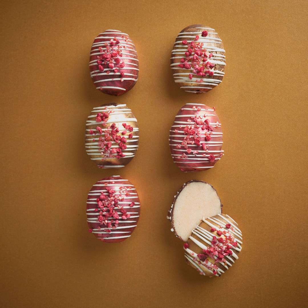 Six pink-and-white decorated marzipan Easter eggs arranged on a brown background