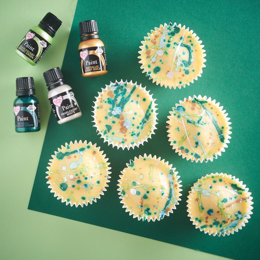 Lemon cupcakes decorated with turquoise sprinkles beside bottles of edible paint