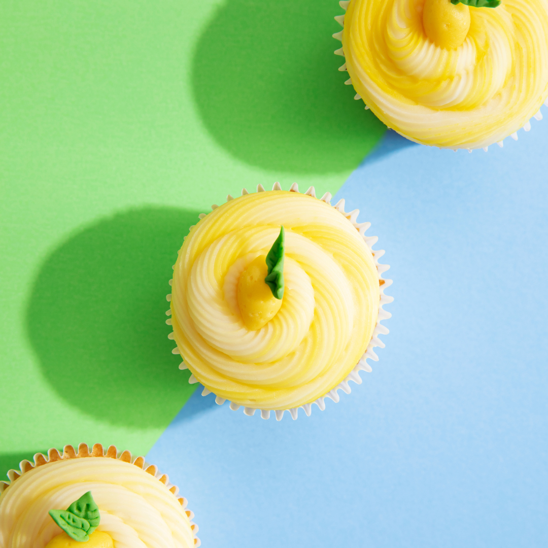 Yellow buttercream cupcakes with lemon-shaped icing decorations on a green and blue background