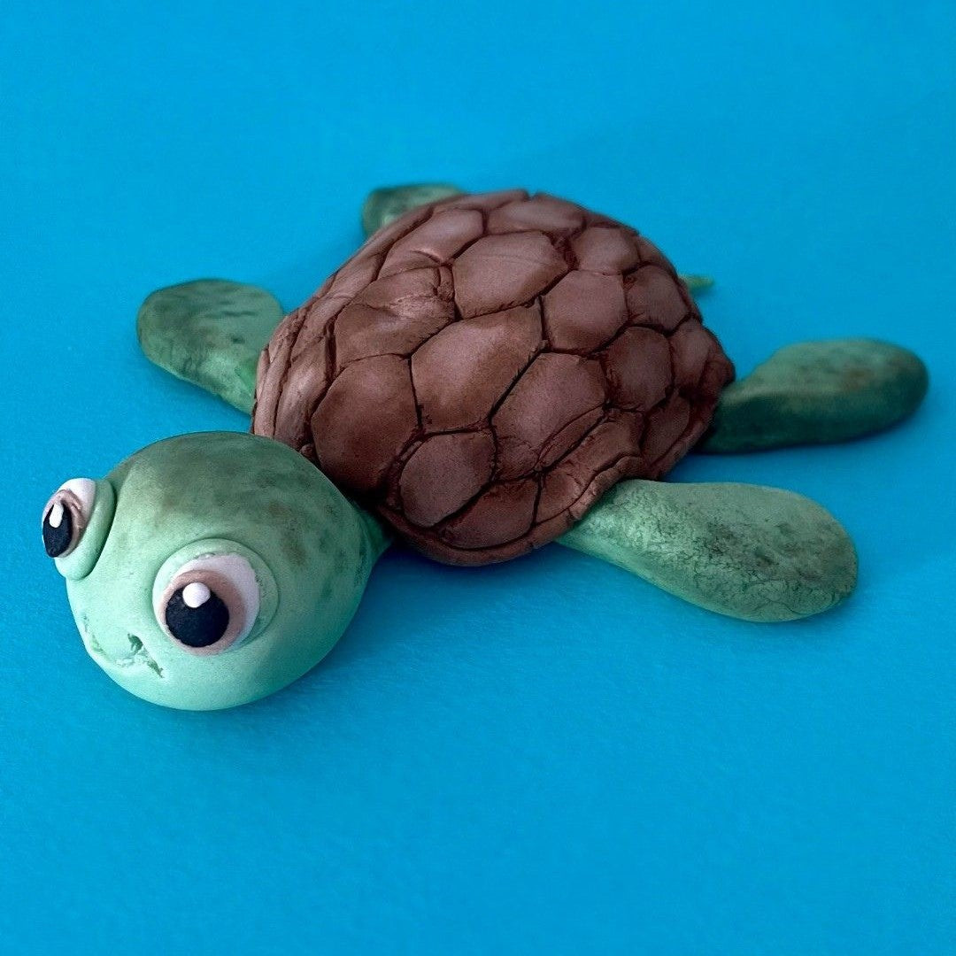 Fondant sea turtle cake topper with a chocolate shell on a blue background