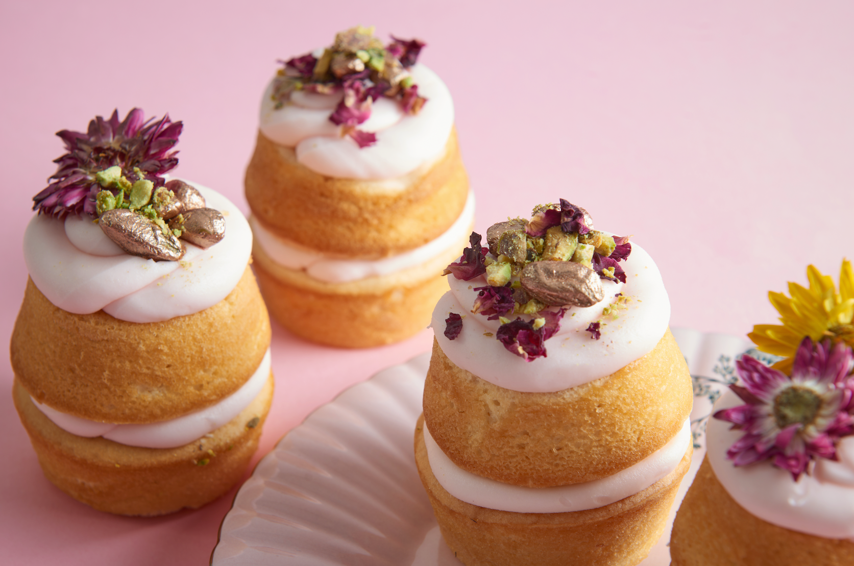 Pistachio mini cakes topped with white icing, chopped nuts and dried rose petals