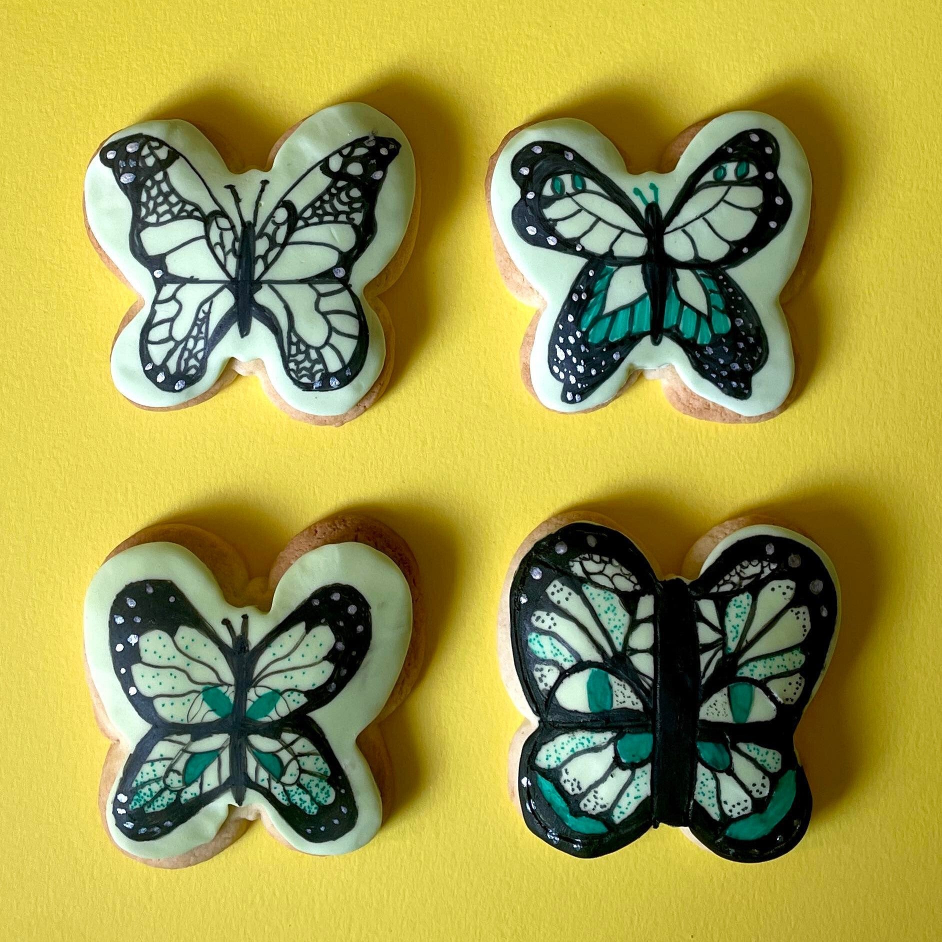 Four butterfly biscuits decorated with black, white and turquoise icing