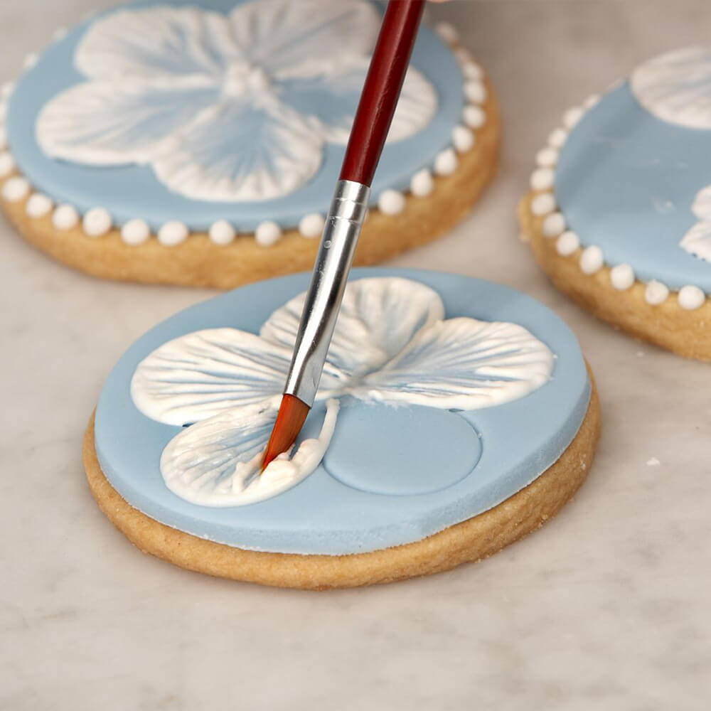 Brushing royal icing to create flower decorations on biscuits